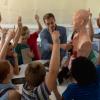 En mannlig lærer peker på en torsomodell som viser kroppens ulike organer. En gruppe barneskoleelever sitter i ring rundt et bord og rekker opp hendene.